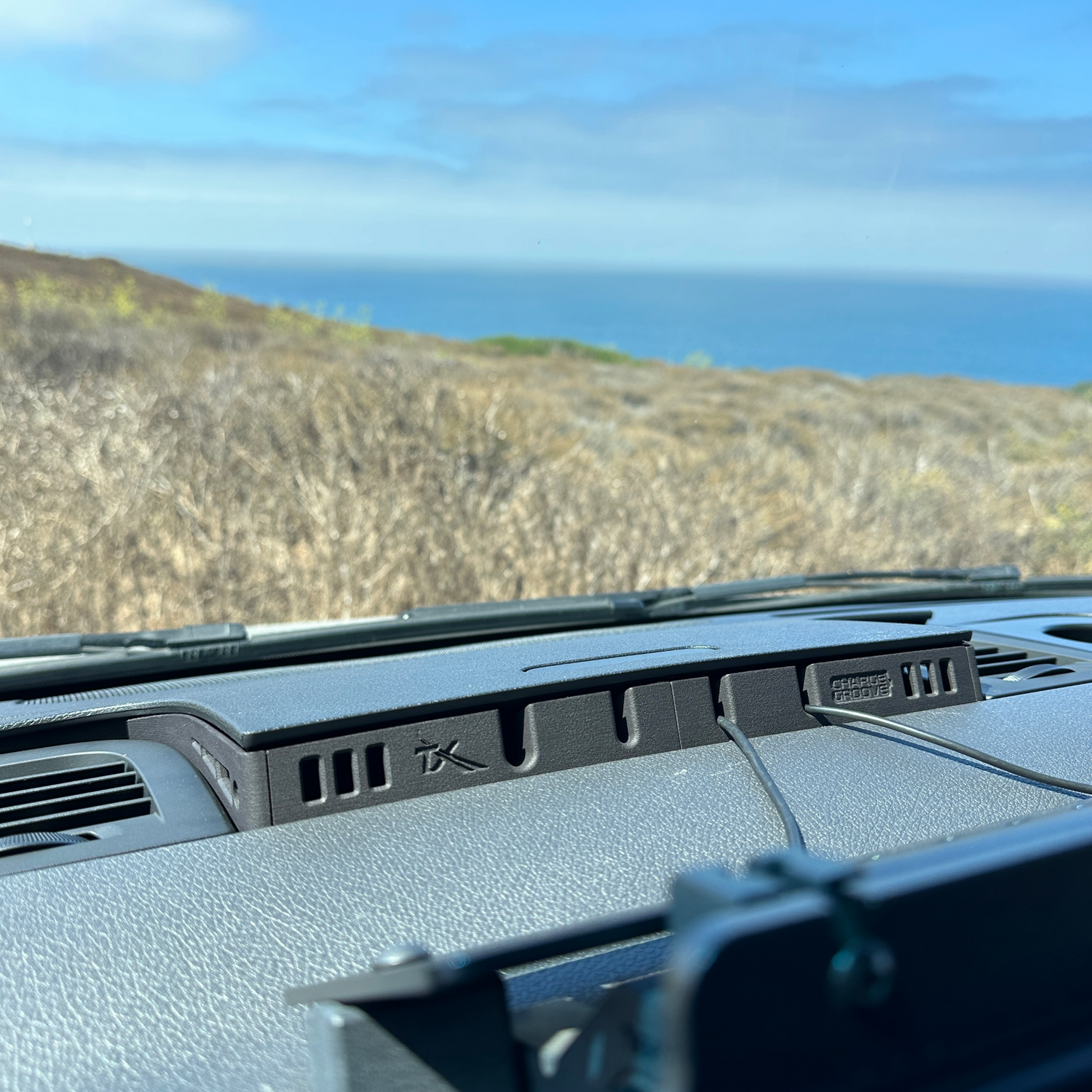 Dashboard phone mount with rugged design installed in vehicle overlooking coastal landscape