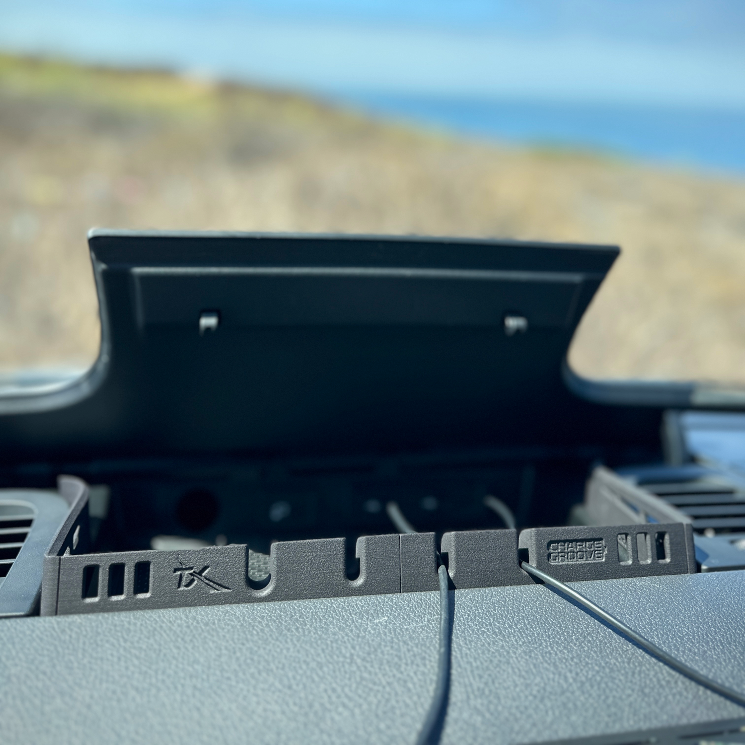 Dashboard organizer tray with cable management slots inside a car with an open compartment lid.