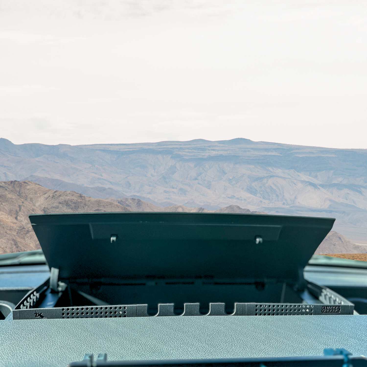 Open dashboard storage compartment inside a vehicle with a scenic mountain view ahead.