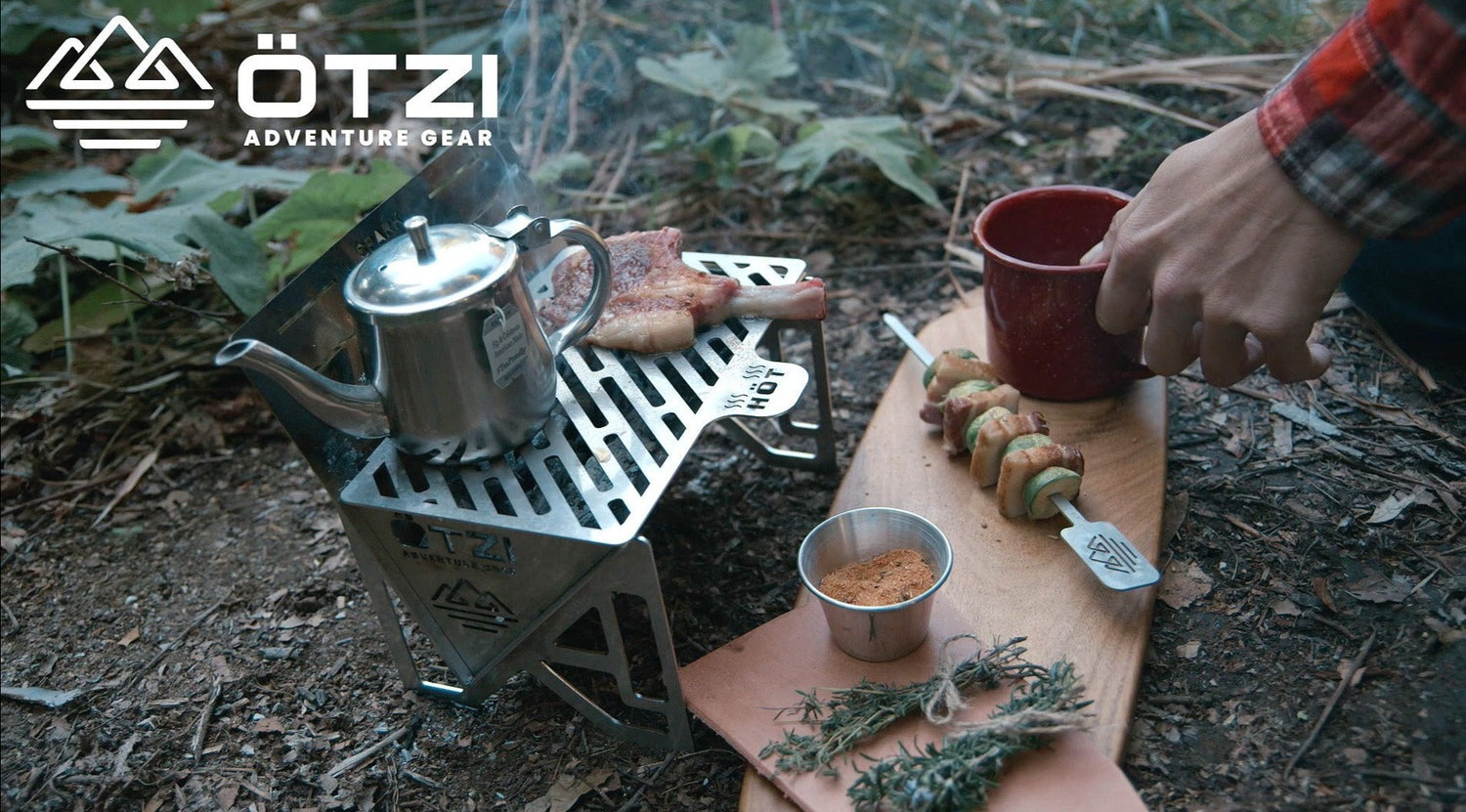 Compact metal camping stove with teapot and food skewers set up in a forest setting