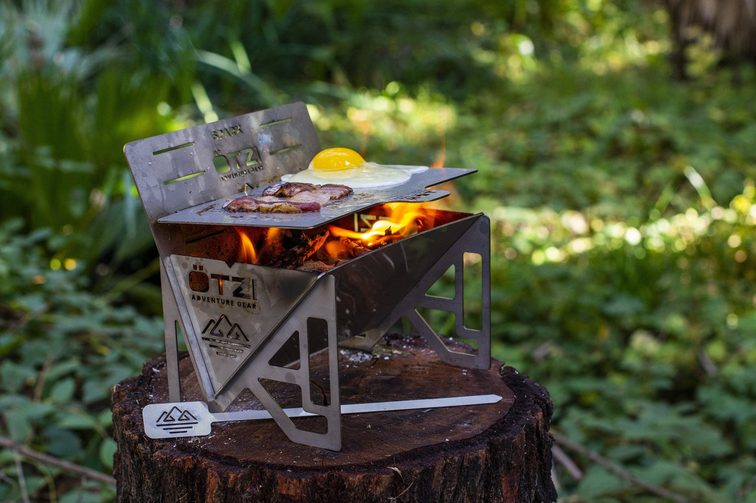 Portable stainless steel camp grill cooking bacon and eggs on a tree stump in the forest