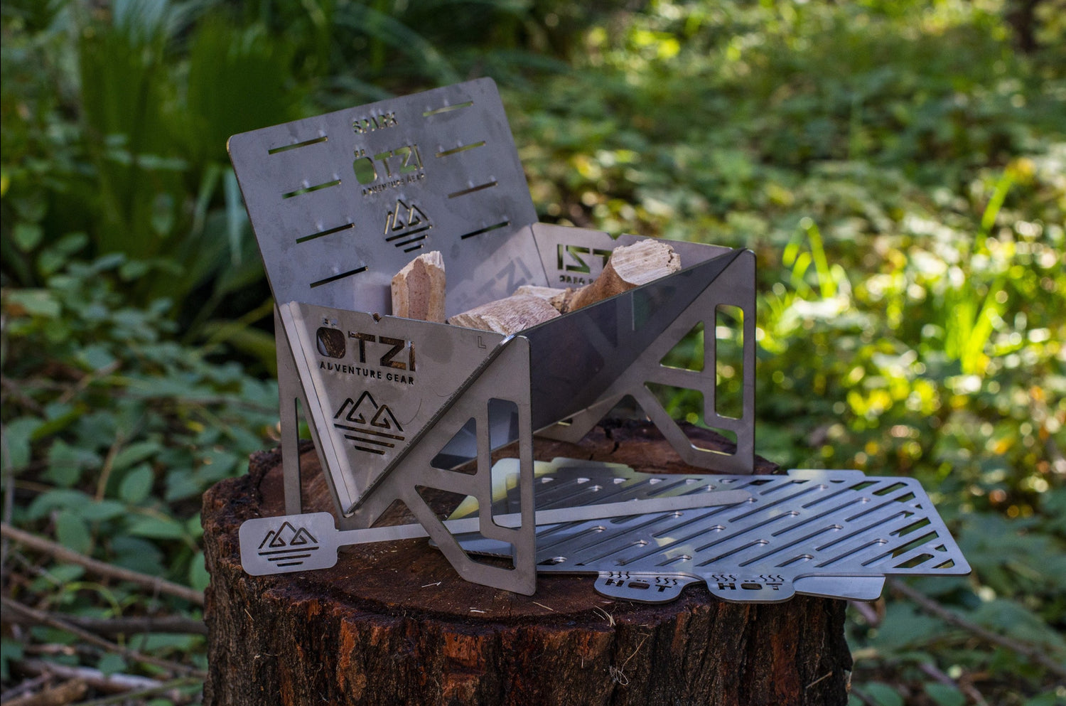 Portable stainless steel campfire stove with wood pieces, set on a tree stump in the forest.