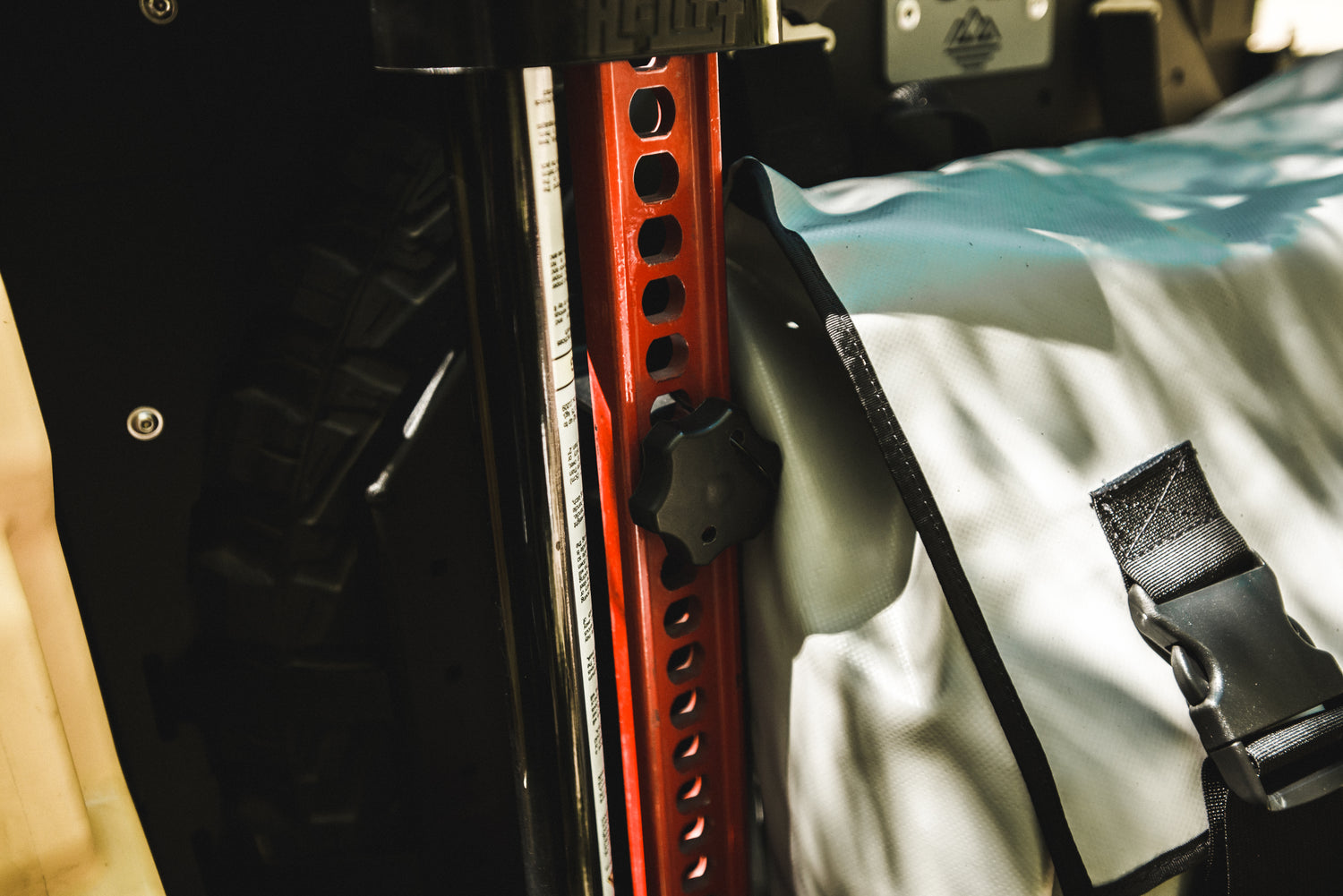 Close-up of a red off-road jack mounted next to a gray gear bag with black buckle straps.