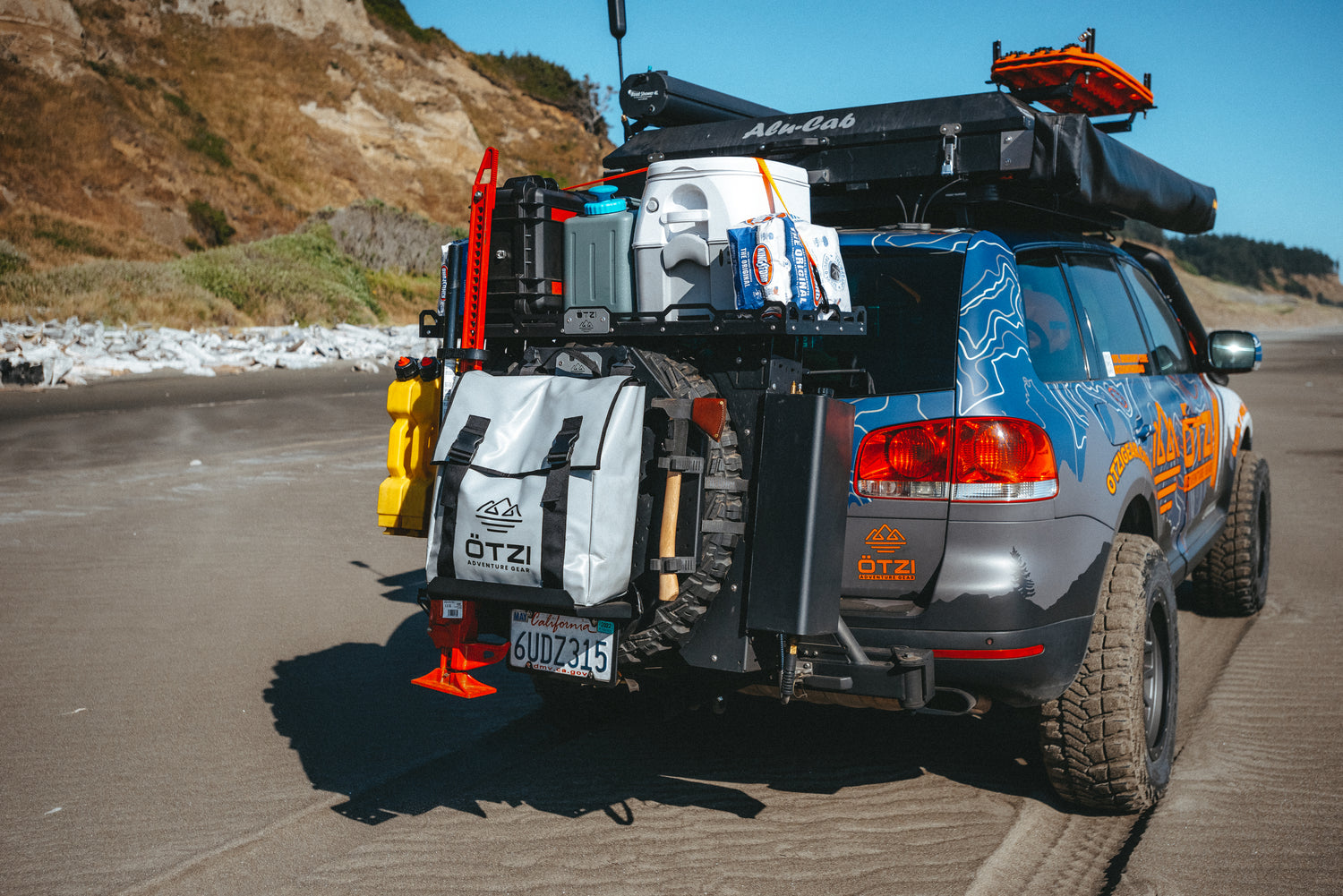 Off-road SUV with camping gear and recovery tools parked on a sandy beach