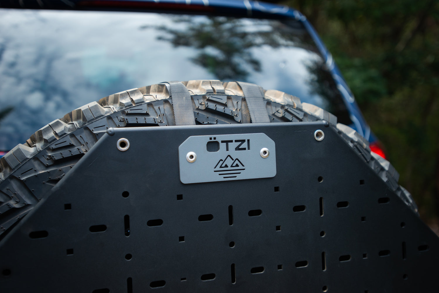Close-up of a spare tire mounted with a black gear panel and ÖTZI logo plate.