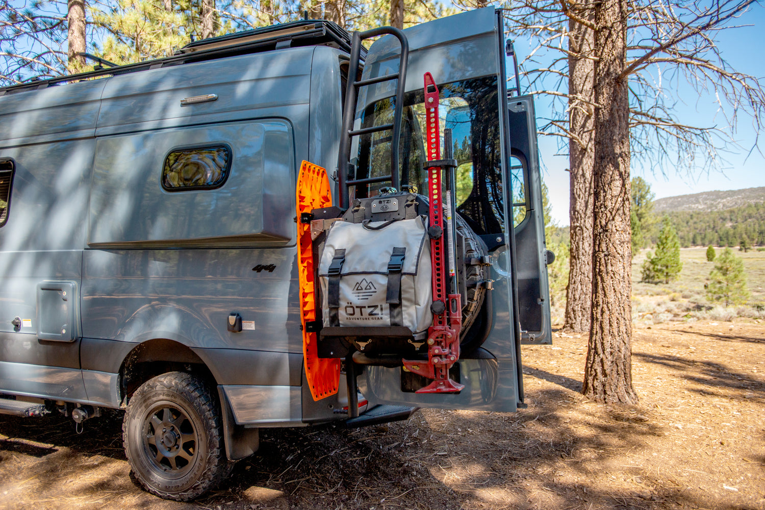 Off-road van with mounted gear including a recovery board, jack, and storage bag in forest setting