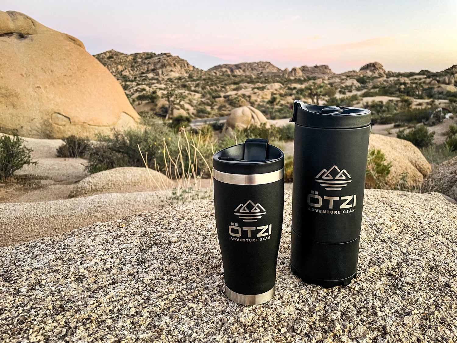 Two Ötzi travel mugs on a rock in a desert landscape at sunset