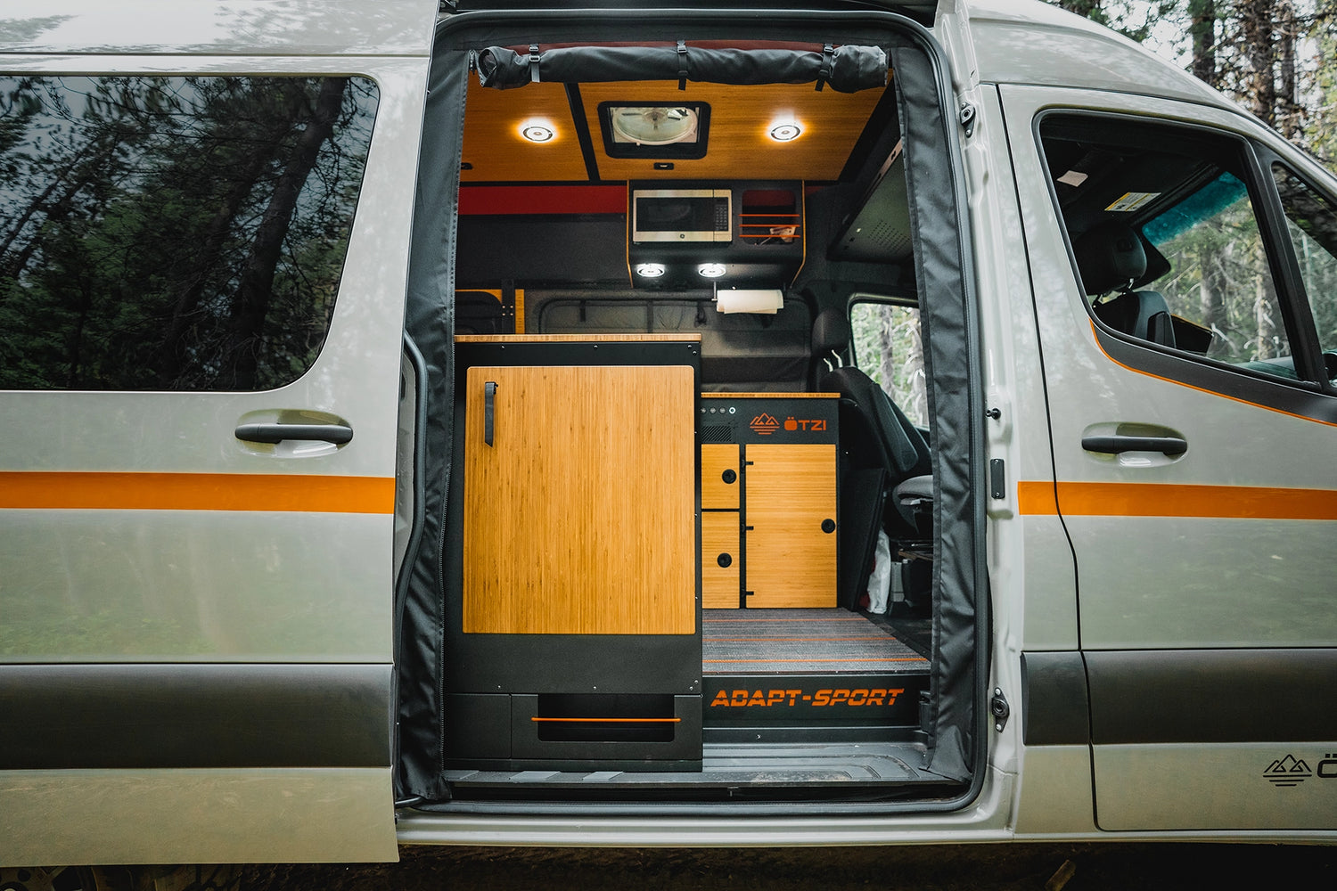 Off‑road camper van parked at a forest campsite, couple enjoying vanlife around the campfire