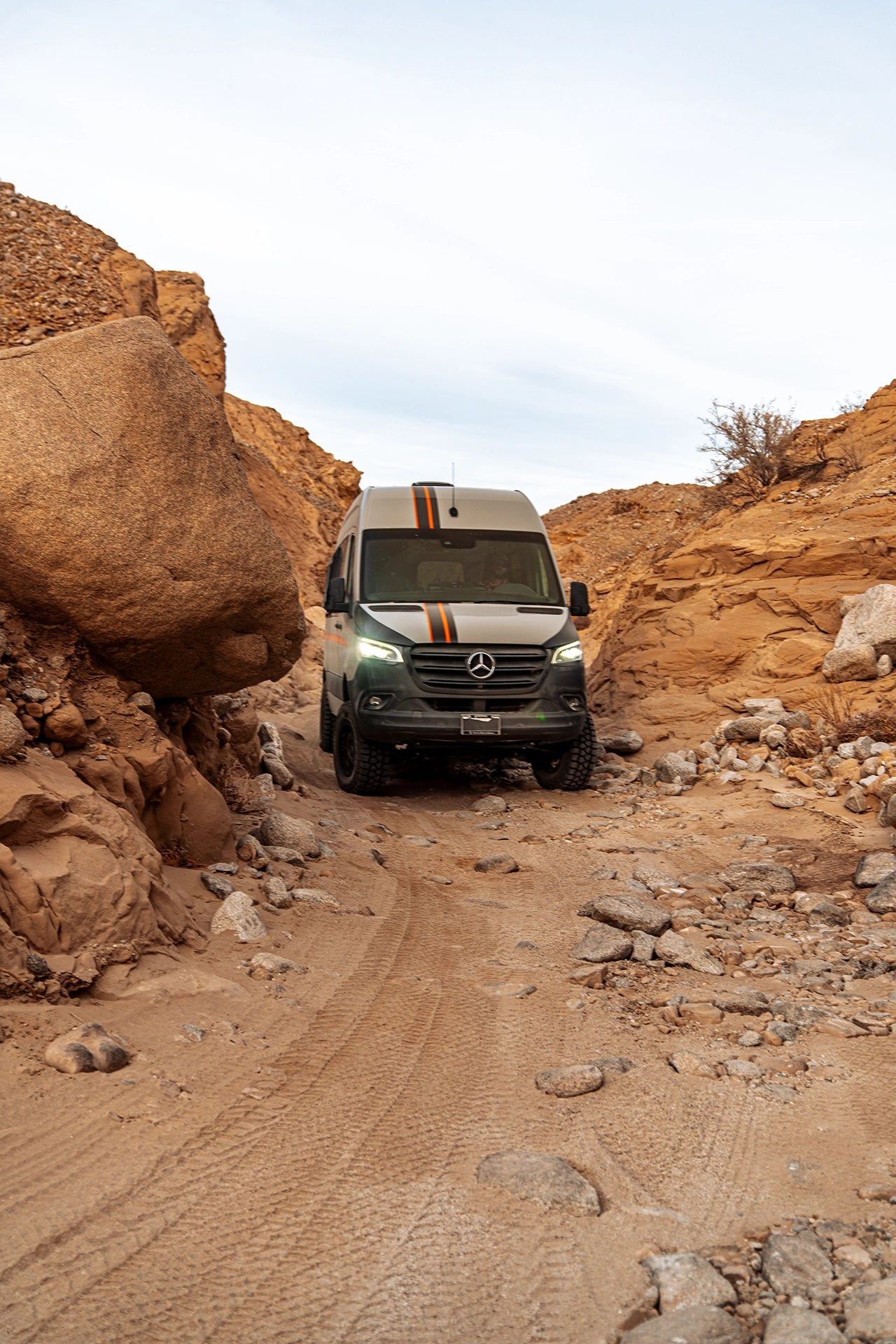 Sprinter off‑road camper van climbing a dirt mountain road on a weekend camping trip