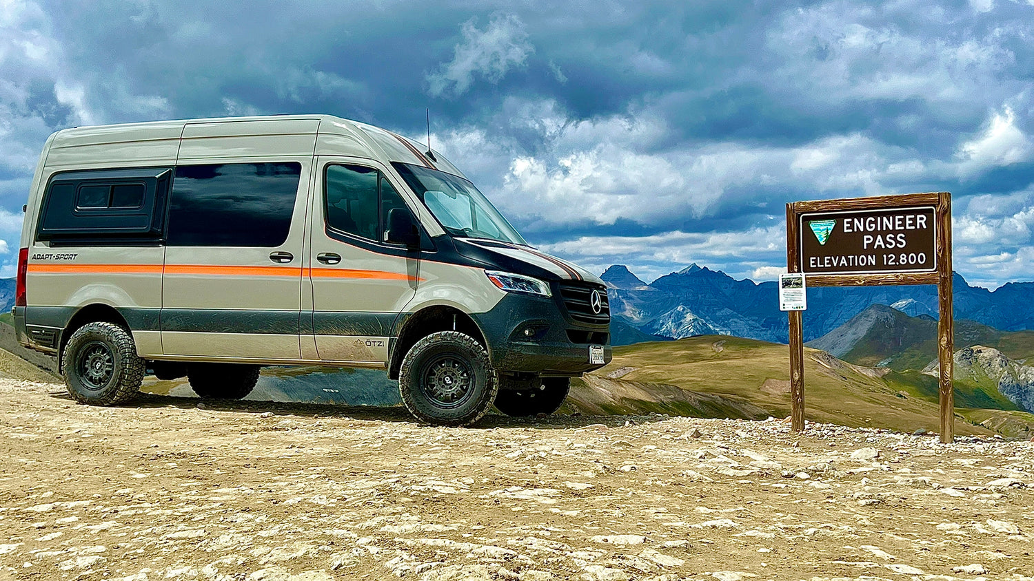 Fully off‑grid adventure van with roof solar panels, roof rack, and rear storage box at remote campsite