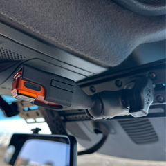 Close-up of a dash-mounted tactical flashlight clipped to a vehicle headliner mount.