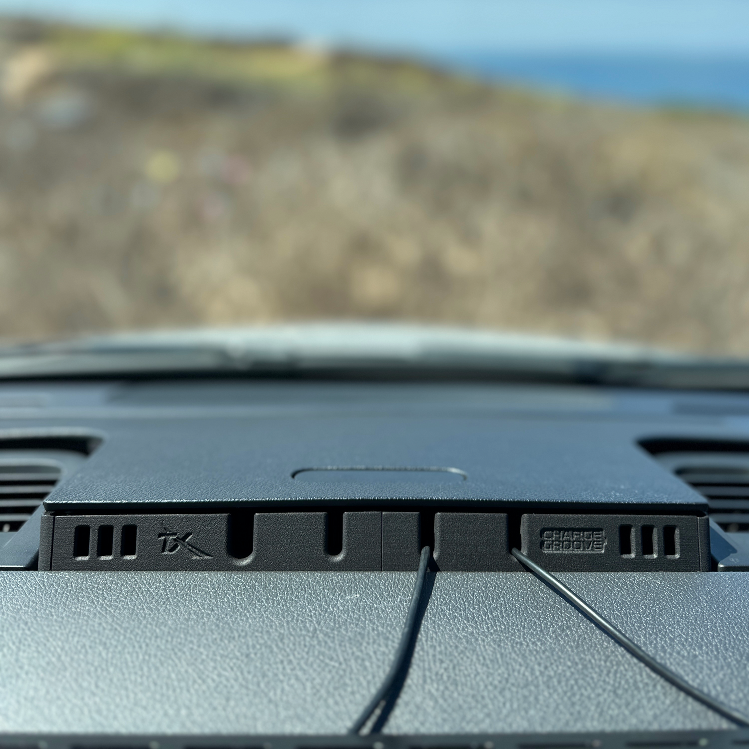 Dashboard-mounted charging station with two connected cables, viewed from inside a car.
