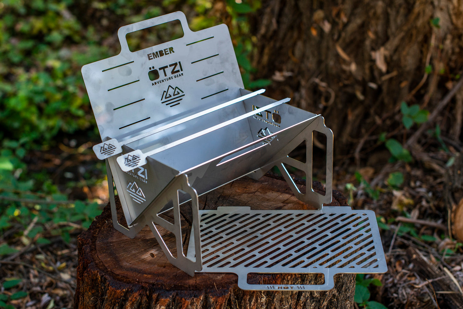 Portable stainless steel campfire grill with foldable legs and removable grate on a tree stump