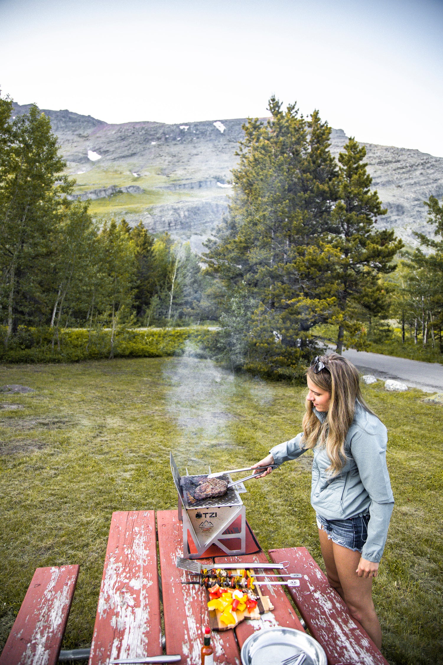 Woman grilling steak on a portable stove at a scenic mountain campsite