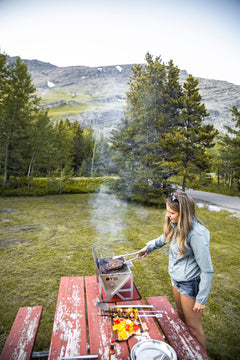 Woman grilling steak on a portable stove at a scenic mountain campsite