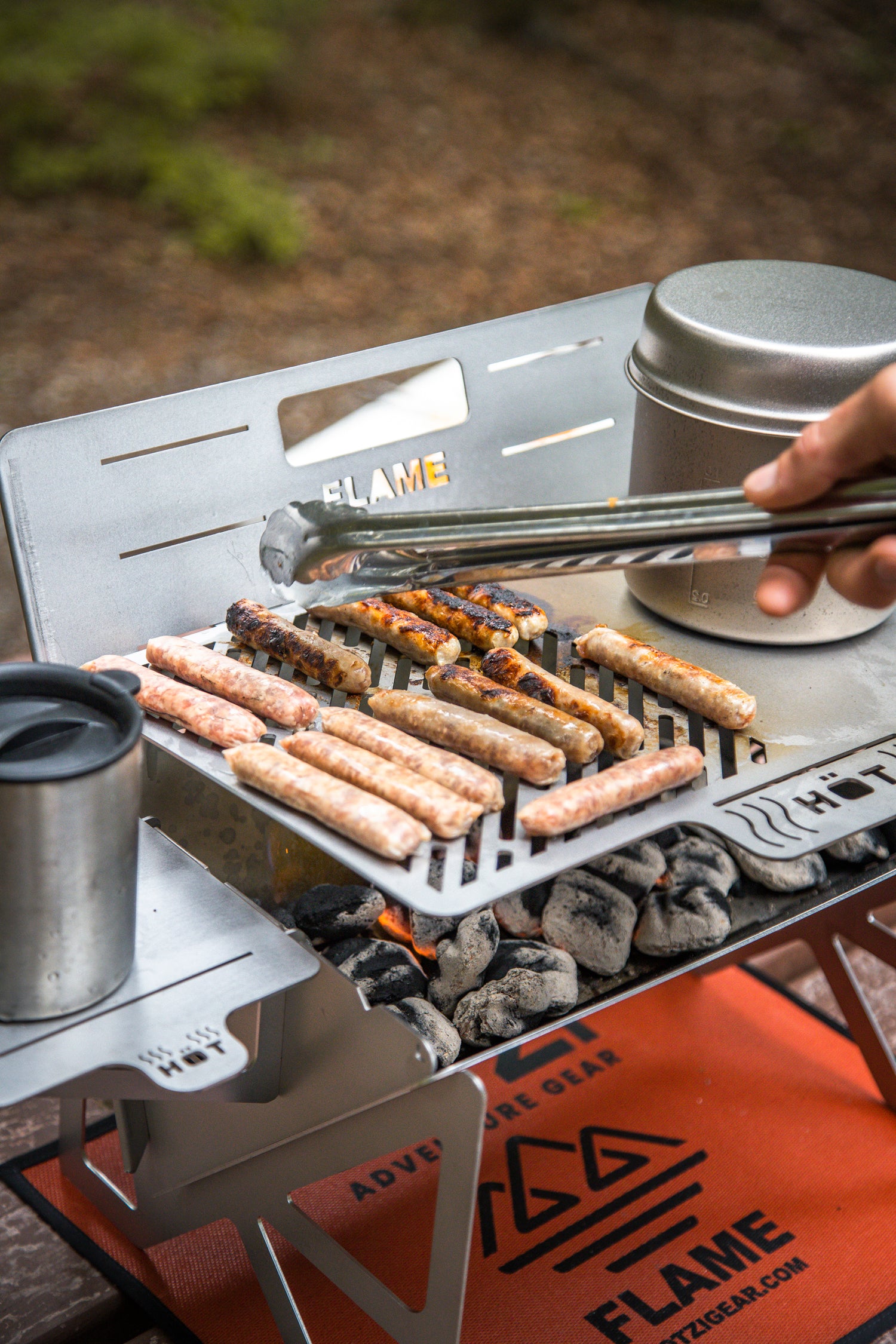 Person grilling sausages over charcoal on a portable camping grill outdoors.