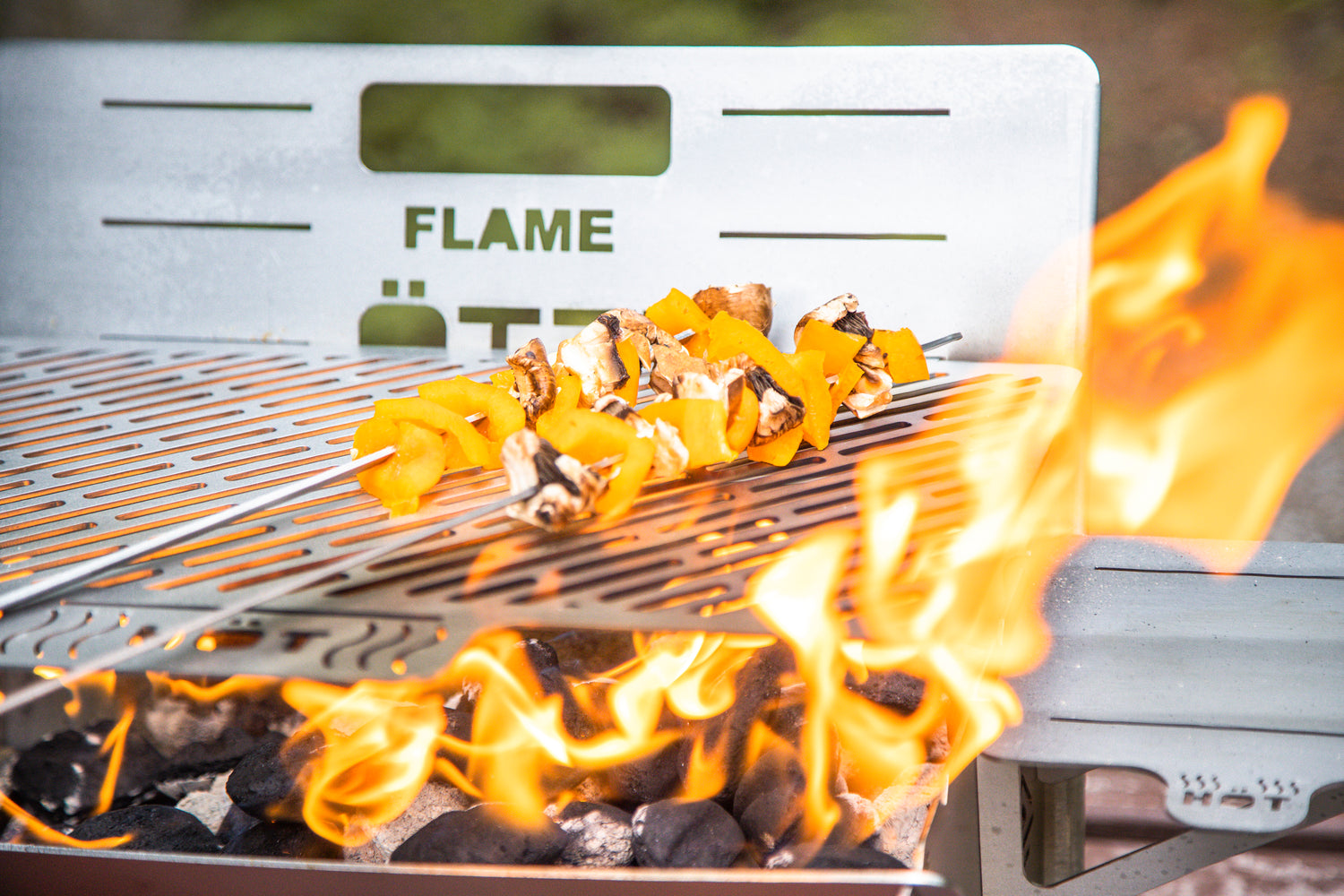 Vegetable skewers with mushrooms and bell peppers grilling over open flame on a metal barbecue grill.