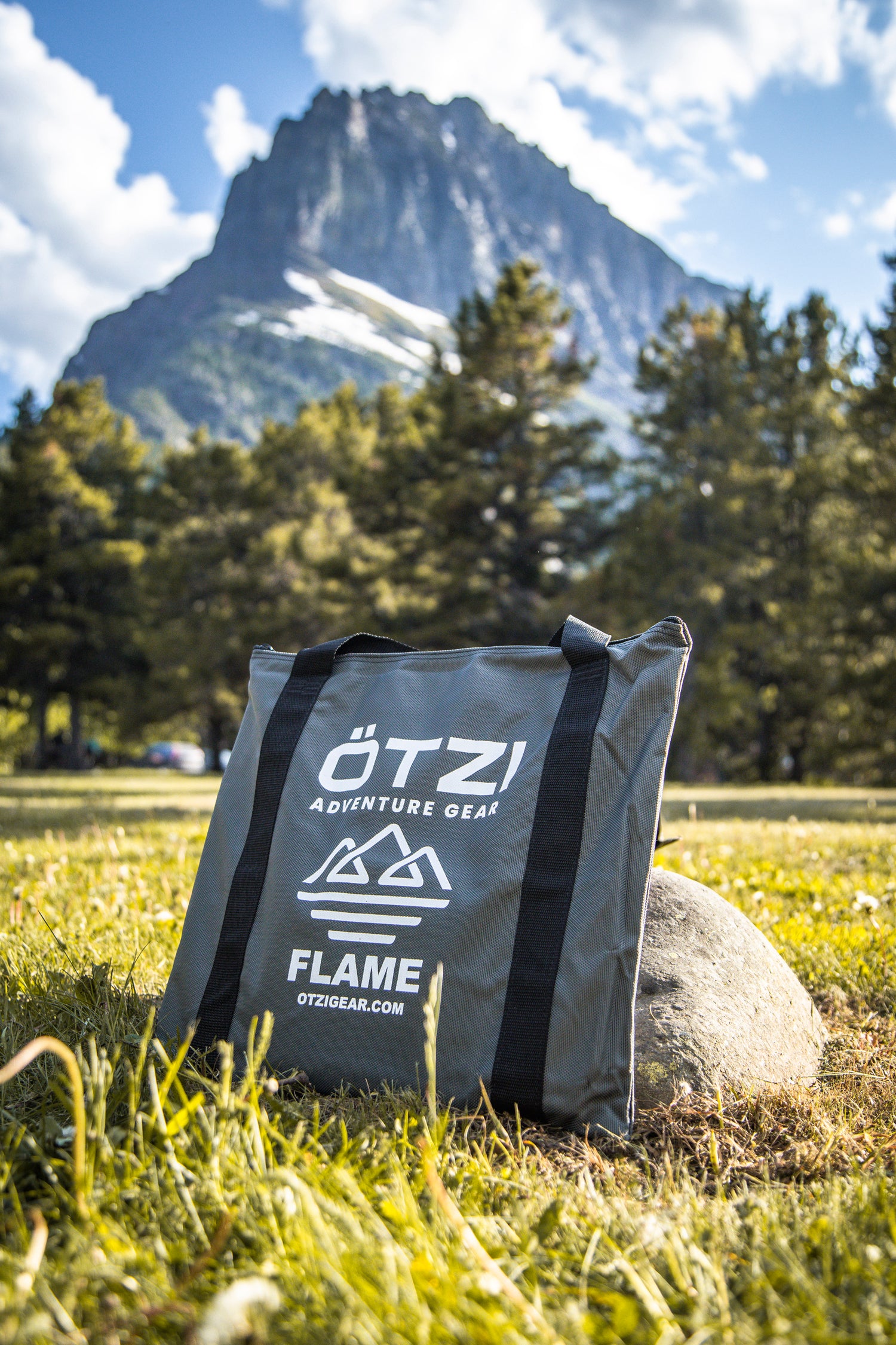 Gray OTZI adventure gear bag leaning on a rock in a scenic mountain landscape.
