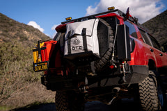 Off-road SUV with ÖTZI gear bag mounted on rear tire carrier in mountain terrain