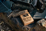 Box of wax-infused jute fire tinder with sticks and camping gear on a rock surface