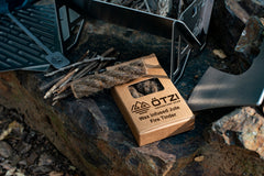 Box of wax-infused jute fire tinder with sticks and camping gear on a rock surface