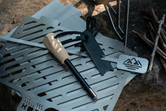 Fire starter kit with ferro rod, striker, and metal grill plate on a rock surface