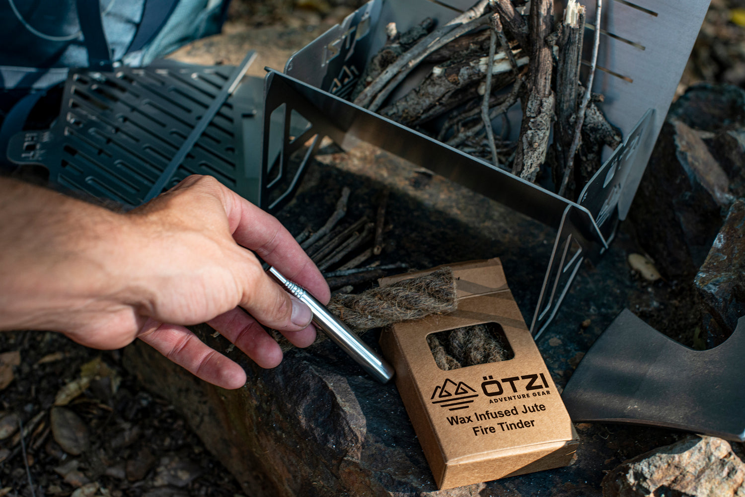 Hand using fire starter with wax-infused jute tinder near a portable camping stove and small twigs.