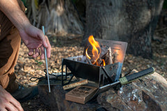 Person tending a compact portable campfire stove with burning wood outdoors