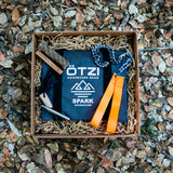 Outdoor survival kit with fire starter, rope, flint, and orange straps in a gift box on fallen leaves