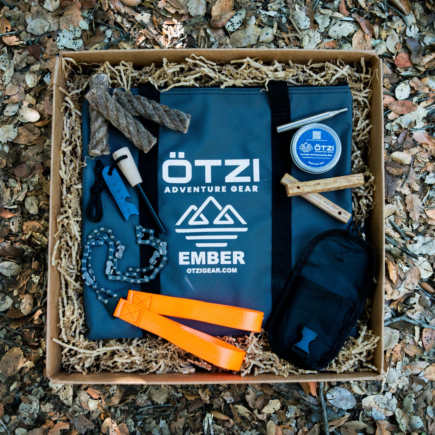 Outdoor survival gear set in a box with tools, fire starter, rope, and carrying pouch.