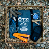 Outdoor survival gear set in a box with tools, fire starter, rope, and carrying pouch.