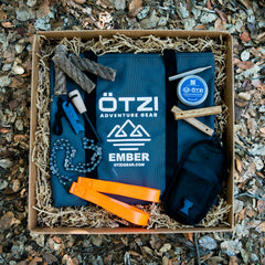 Outdoor survival gear set in a box with tools, fire starter, rope, and carrying pouch.