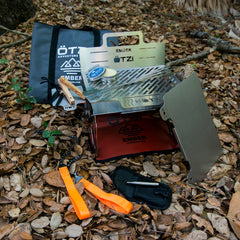 Portable stainless steel camping stove kit with accessories displayed on forest floor
