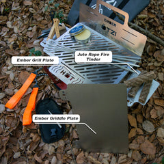 Outdoor cooking kit with Ember grill and griddle plates, jute fire tinder, tools, and accessories on forest floor