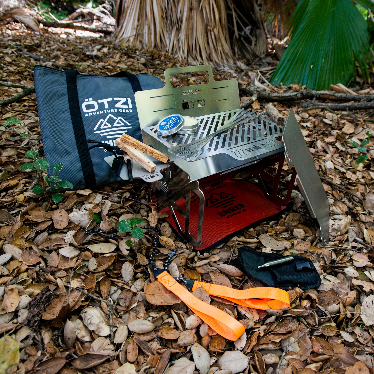 Portable stainless steel camping grill set with accessories on forest floor.