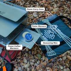 Outdoor fire pit set with carry case, skewers, coffee warmers, and seasoning wax on leaf-covered ground