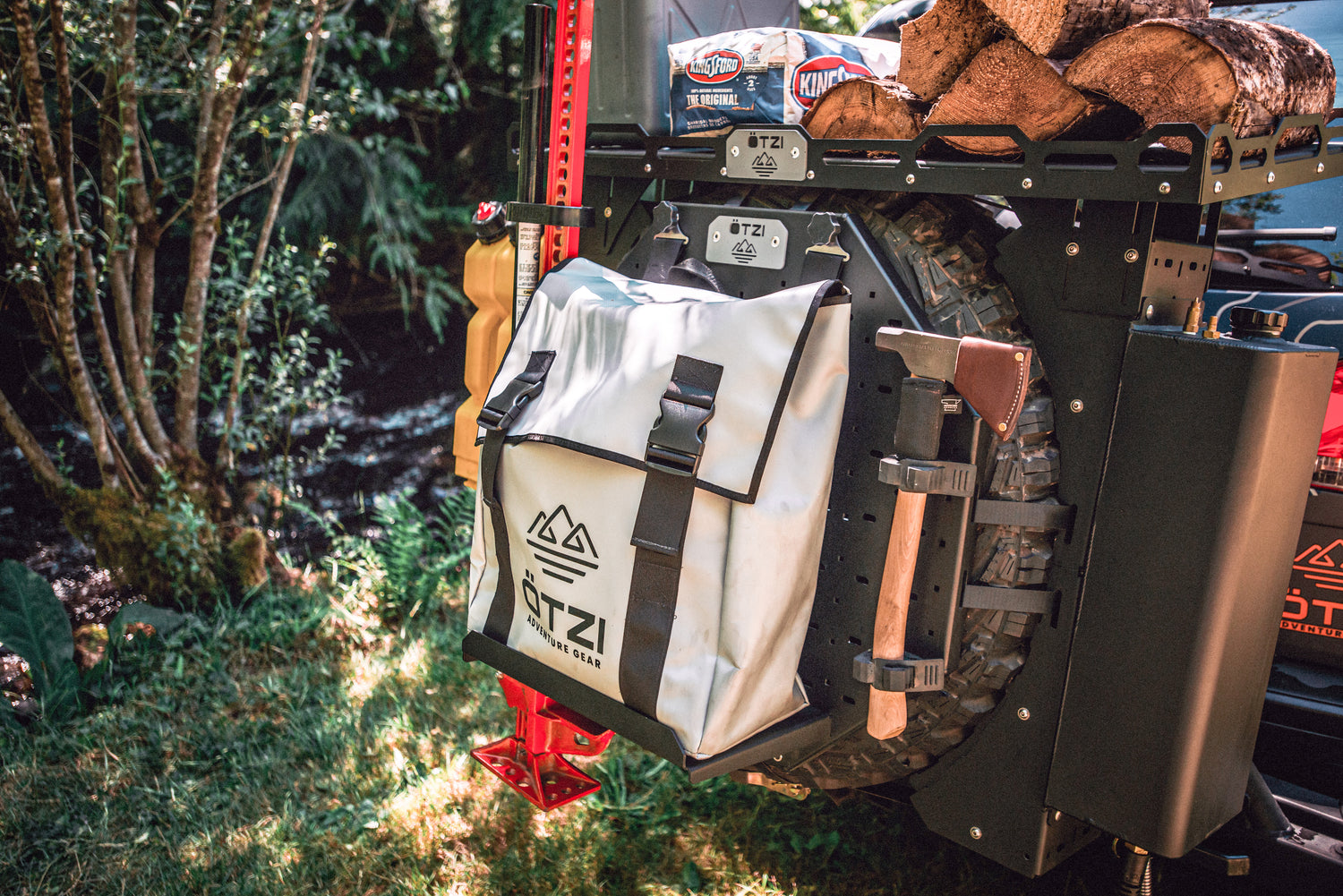 Overland gear mounted on a vehicle’s spare tire including a white storage bag, axe, and firewood.