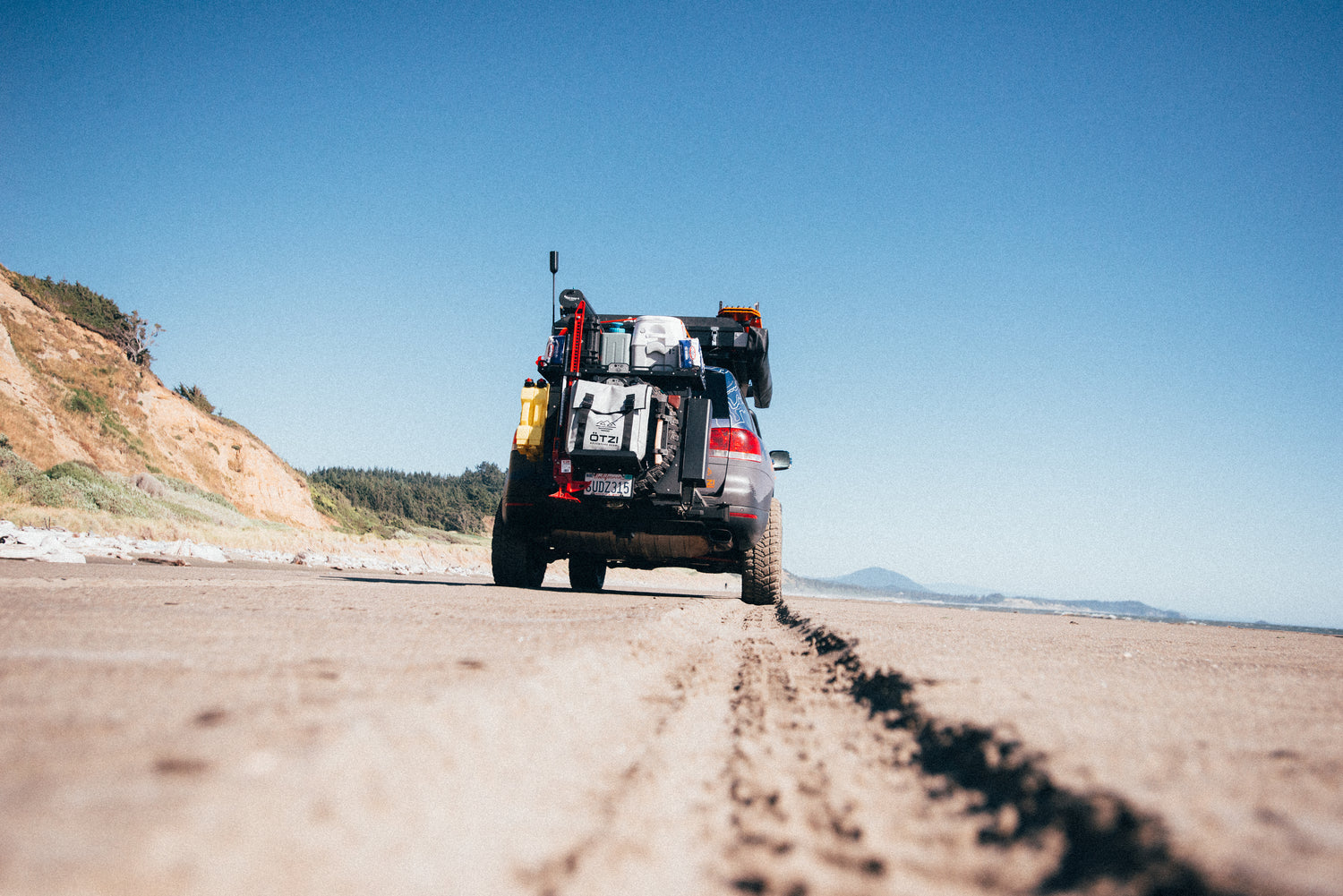 Off-road SUV parked on sandy beach with camping gear on the back
