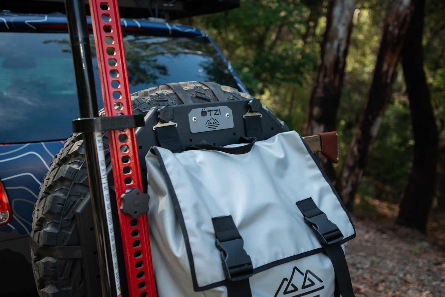 White off-road gear bag mounted on a spare tire with forest in the background