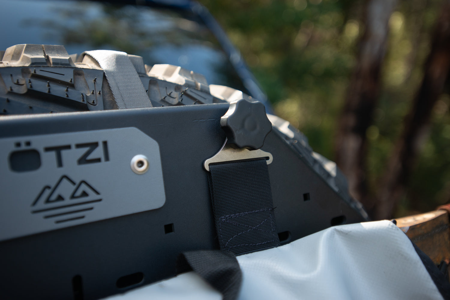 Close-up of a mounted off-road tire with a strap and metal latch secured on a gear panel.