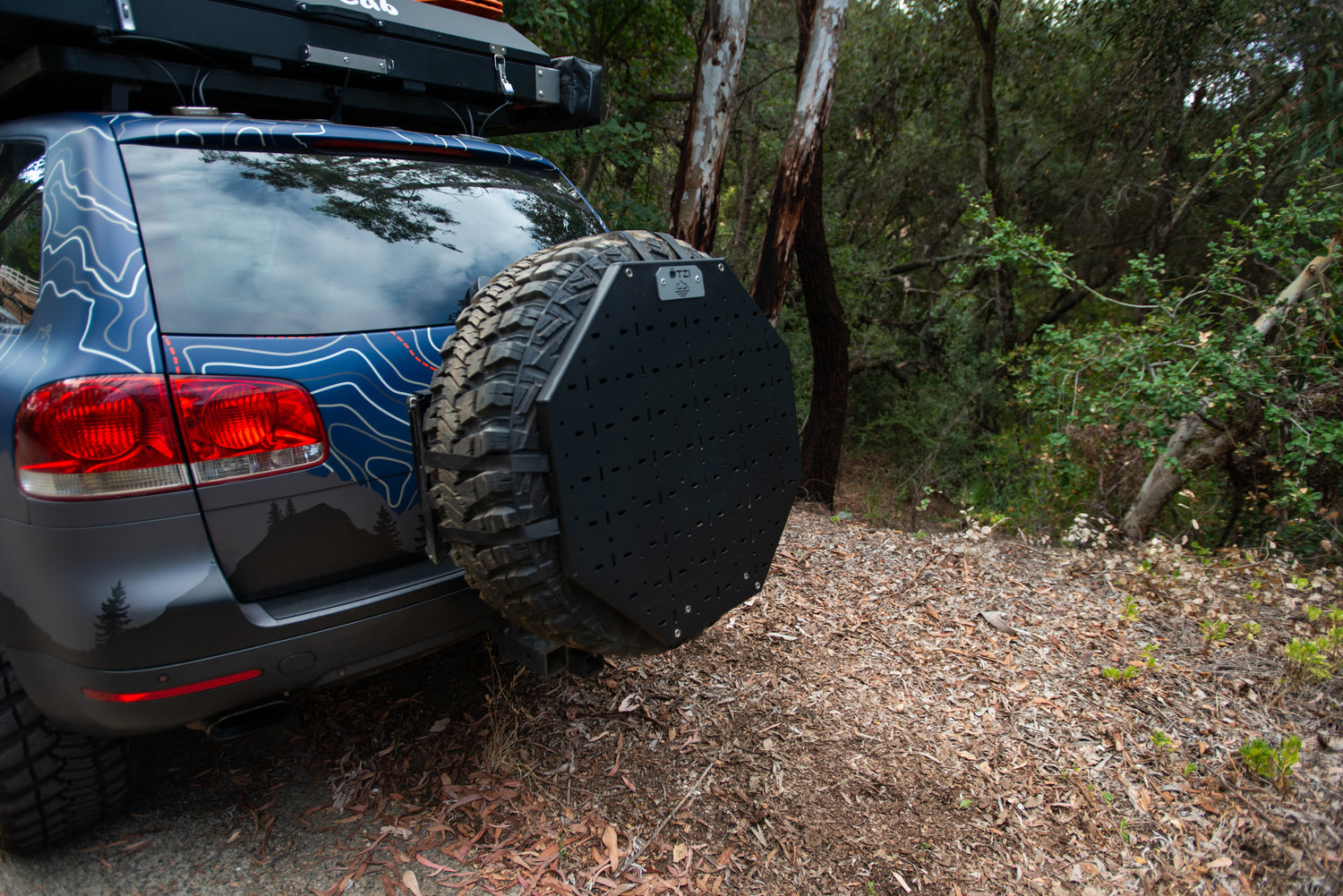 Off-road SUV with a rear-mounted spare tire carrier parked near a forest trail