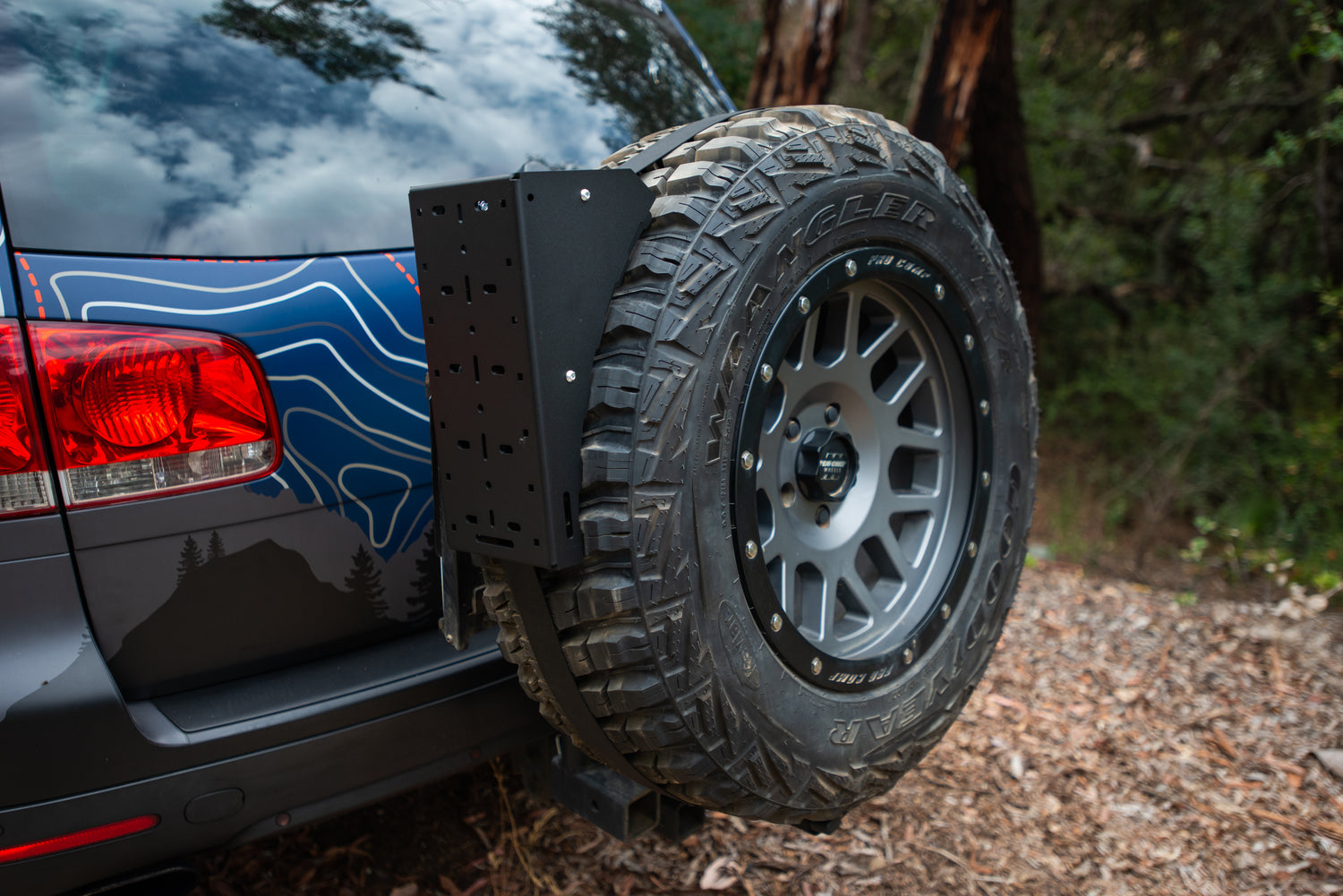 Rear-mounted spare tire on SUV with off-road tire carrier in wooded area