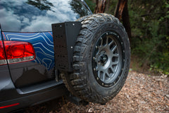 Rear-mounted spare tire on SUV with off-road tire carrier in wooded area