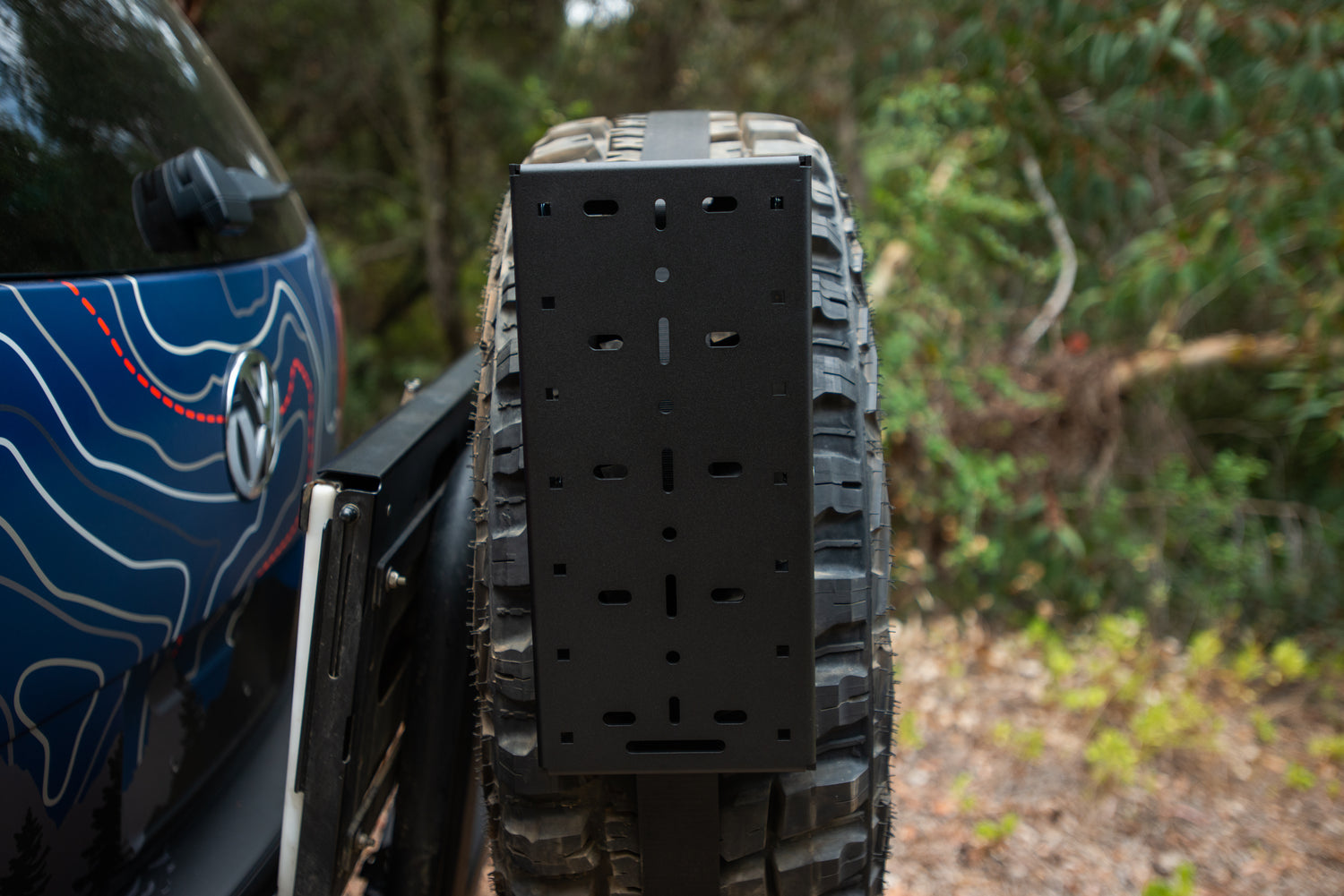 Black metal mounting plate attached to spare tire on off-road vehicle.