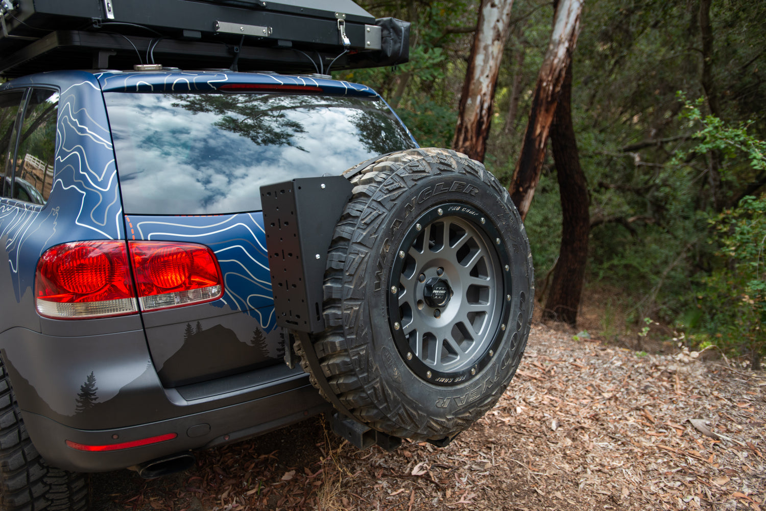 Off-road SUV with spare tire mounted on swing-out hitch in forest setting