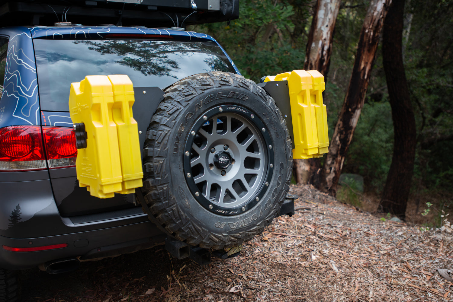 Rear view of an off-road vehicle with a spare tire and two yellow fuel canisters mounted on the back.