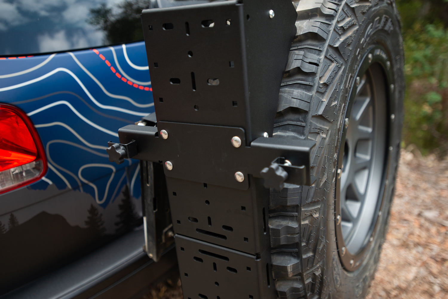 Close-up of a spare tire mounted on a black off-road tire carrier attached to a vehicle.