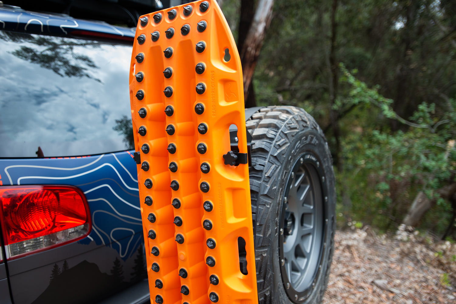 Orange off-road recovery board mounted on rear spare tire of SUV in forest