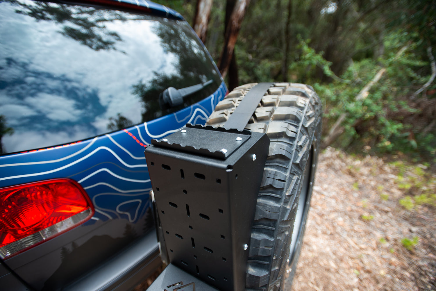 Close-up of a rear tire carrier mounted on an off-road SUV in a wooded area