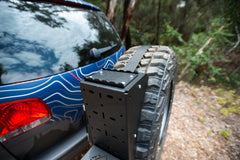 Close-up of a rear tire carrier mounted on an off-road SUV in a wooded area